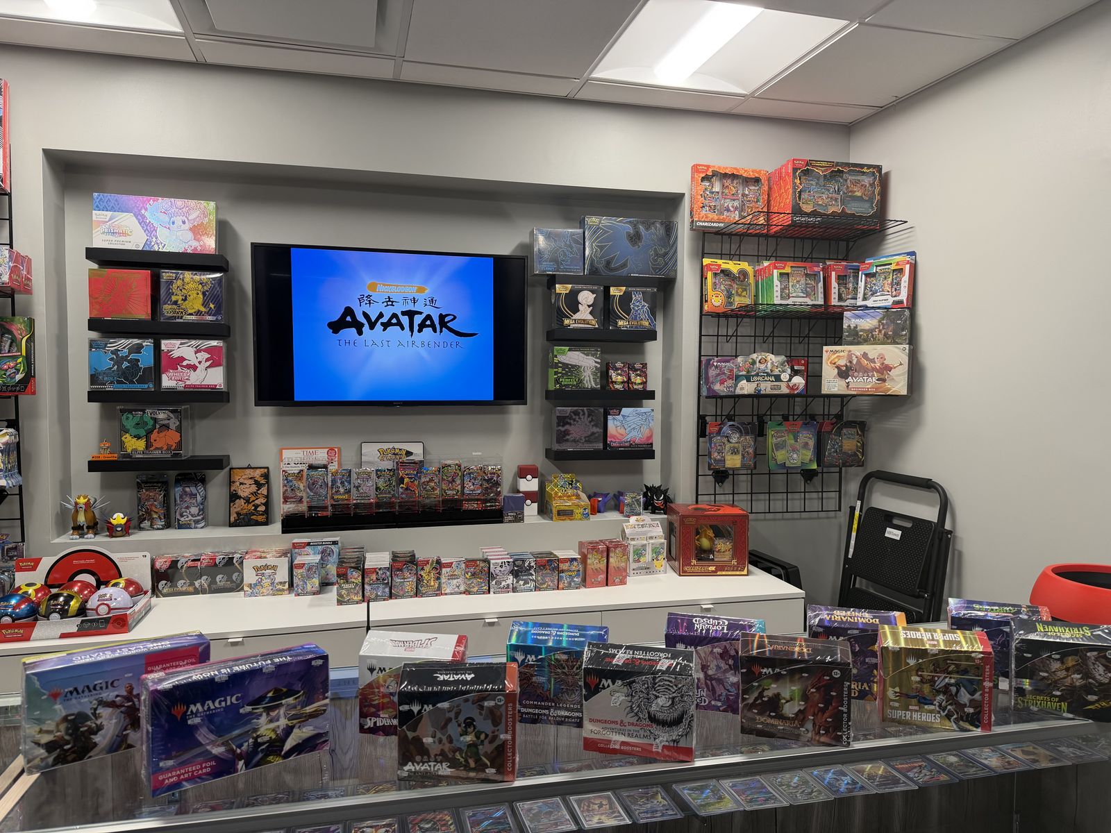 Sealed Magic: The Gathering, Disney Lorcana, One Piece, and other card games lined up on the shop counter beside a glass case of singles